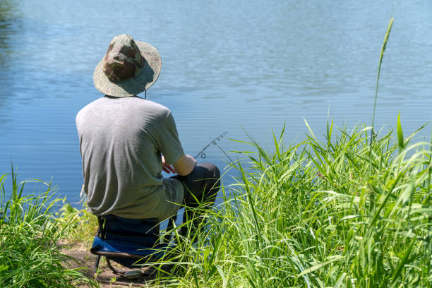 istock Fisherman in a hat is fishing on a forest lake or river 1255972964