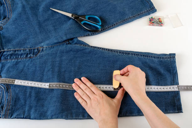 caucasian woman hands measure the desired length with a measuring tape on a white table. shorten the jeans with scissors and sewing pin. diy summer clothes. - short cut imagens e fotografias de stock