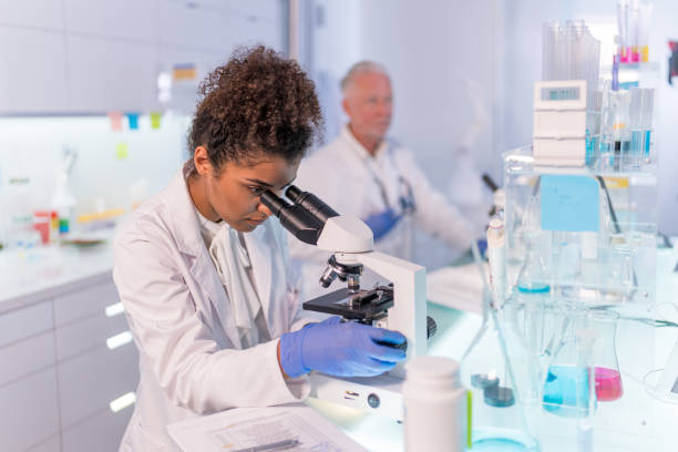 Multi ethnic laboratory team at work. Female doctor loving her job. African ethnicity female doctor using microscope and enjoying her work. Senior adult doctor working in foreground. Futuristic laboratory powered exoskeleton photos stock pictures, royalty-free photos & images