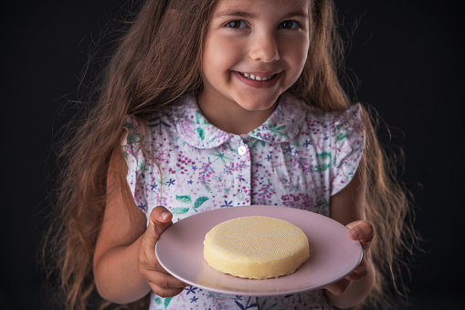 Beautiful little girl surprised from a tasty cheesecake. Kid ready to eat cake.