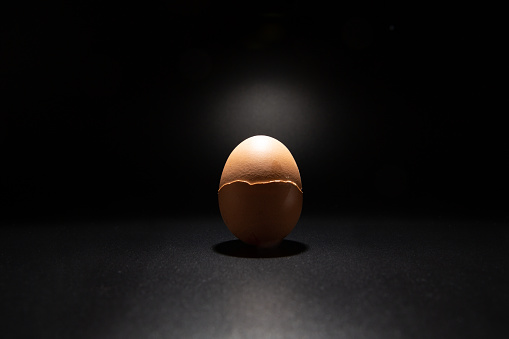Broken chicken eggshell isolated on black background with copy space. Light filters through the cracks.