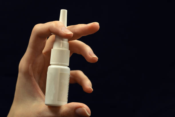 istock woman's hand holds a nasal spray in a white bottle close-up on a black background, copy space 1255991644