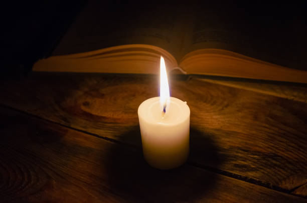 istock burning candle and a book on a table in the dark on a wooden table. Concept of knowledge, religion, magic 1255992005