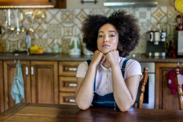 istock Lonely young woman sitting in the kitchen alone and sad looking at camera 1255992643