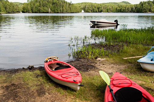 Kayak and boat resting on a calm lake in nature. No people. Horizontal full length outdoors shot with copy space. Back view.