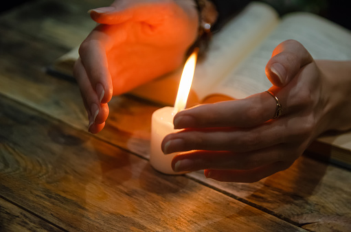 Hands near the candle and a book on the table. Concept of magic, education