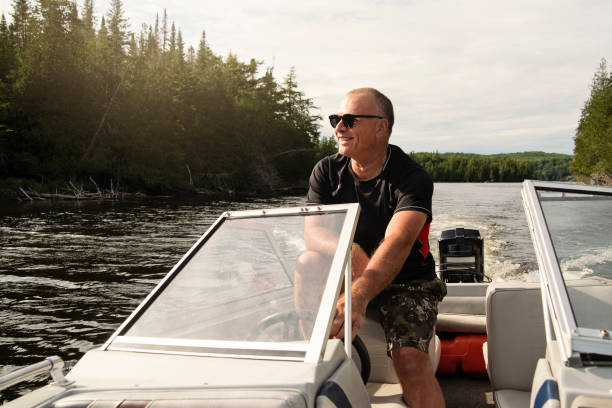 50 + hombre conduciendo barco pequeño en un lago. - laurentian moutains fotografías e imágenes de stock