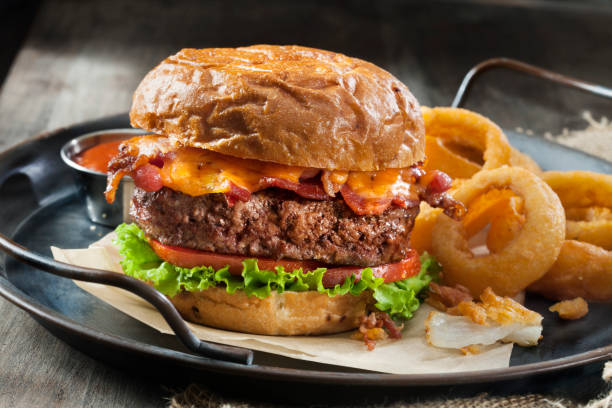 Bacon and Cheddar Burger with Lettuce, Tomato and Thick Cut Onion Rings on a Toasted Onion Bun Bacon and Cheddar Burger with Lettuce, Tomato and Thick Cut Onion Rings on a Toasted Onion Bun bacon cheeseburger stock pictures, royalty-free photos & images