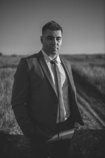 istock Young man in suit standing on dirt road through fields 1256002993