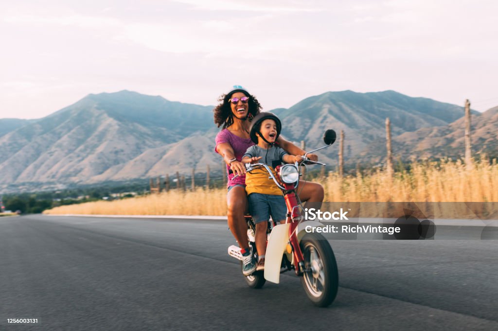 Mother and Son Riding on Retro Scooter A mother and son enjoy a summer ride on a rural Utah road. They are loving the carefree, fresh air of the afternoon sun. Road trip. Family Stock Photo