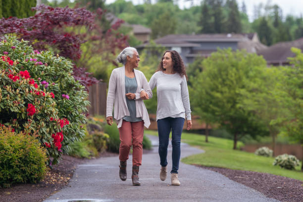 Senior woman and her adult daughter enjoying the outdoors together during Coronavirus A senior woman links arms with her millennial Eurasian daughter as they happily walk through a natural parkland area and enjoy their time together. legacy concept photos stock pictures, royalty-free photos & images