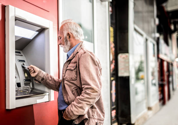 homme aîné insérant une carte de crédit dans le distributeur automatique de atm. - distributeur automatique photos et images de collection