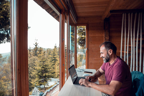 Man working from home Close up of a mid adult man working on a laptop from his cabin in the woods remote location stock pictures, royalty-free photos & images