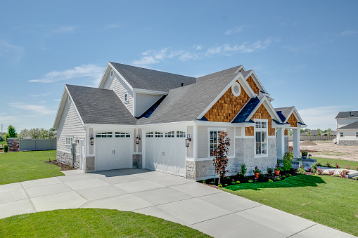 The rear view of a large gray craftsman new construction house with a landscaped yard and a garage and driveway.