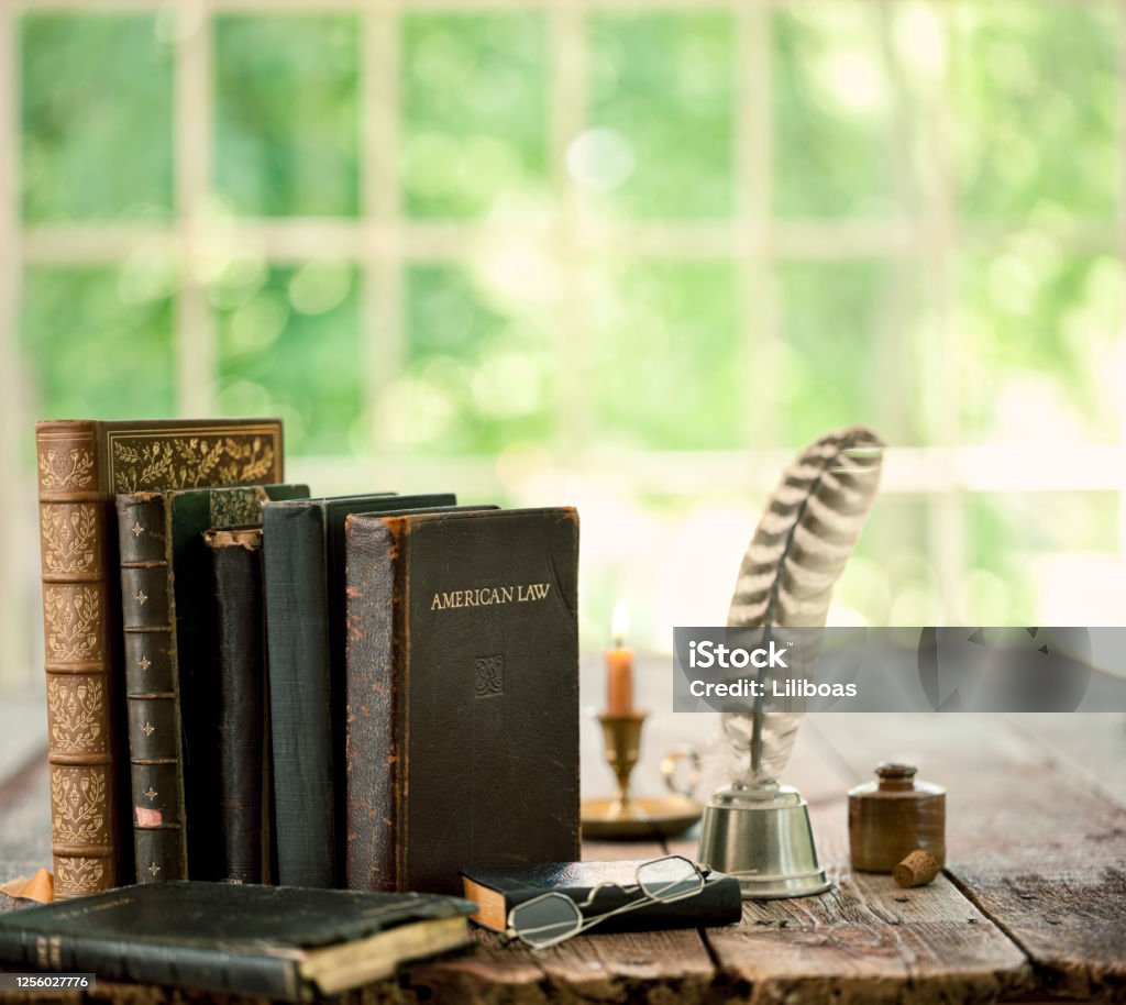 Vintage Books on an Old Wood Table Vintage study area with books, quill pen and candle on an old wood desk in front of a window Ink Well Stock Photo