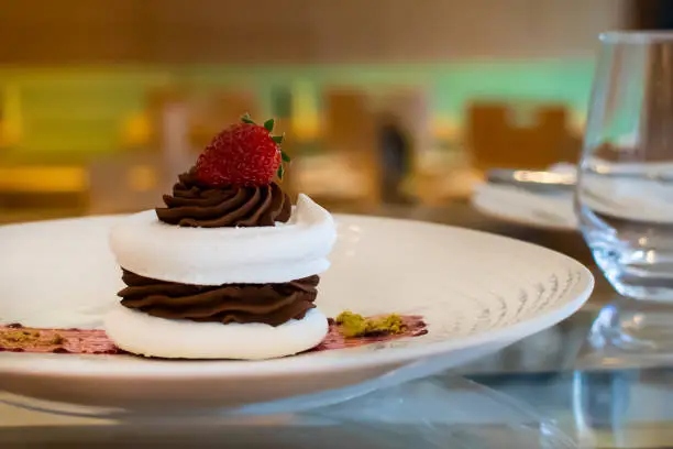Meringue cake with dark chocolate and strawberry on top, in arestaurant setting, with blurred background