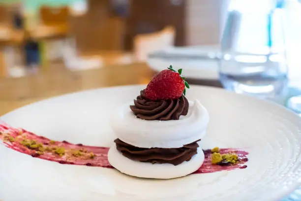 Meringue cake with dark chocolate and strawberry on top, in arestaurant setting, with blurred background