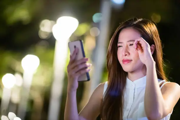 Asian woman use smart phone in the evening and she has eyes fatigue outdoor
