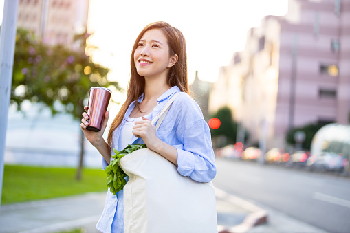 asian woman use reusable eco-friendly ecological cup to drink while commuting in the city
