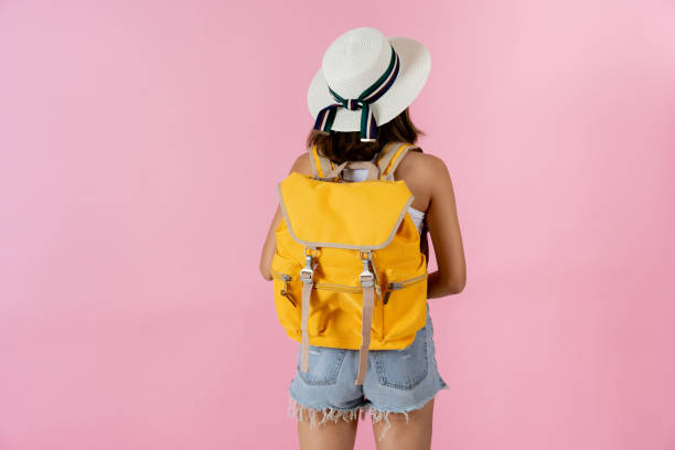 Young woman wearing hat and backpack against pink background