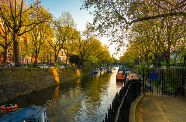 View of Regent's Canal in London, England, in autumn at sunset Beautiful view of Regent's Canal in London, England, with moored and moving boats at sunset in autumn; blue sky and a bridge in background regents canal stock pictures, royalty-free photos & images