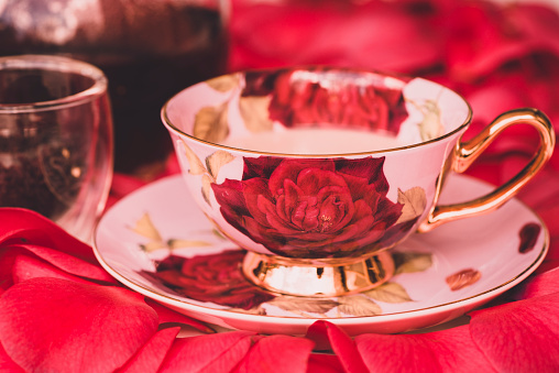 Deep red coloured image of a fancy cup of tea in a rose teacup with tea leaves and teapot our of focus in the background