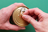 The hand of an adult holds a can of canned food, the second hand pulls the key. Top view on green background, close-up