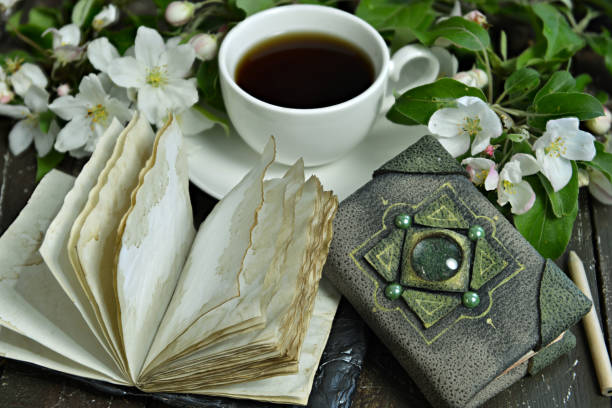 Open diary book with cup of tea and blooming apple tree branches on table.