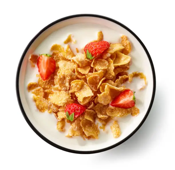bowl of cornflakes with milk and strawberry pieces isolated on white background, top view