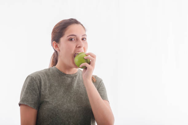 istock beautiful young woman biting a delicious looking green apple while looking at the camera. 1256059235