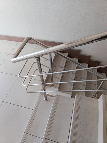 modern design of stanless steel pipes handrail and ceramic tiles staircase in abstract public building, wide angle picture