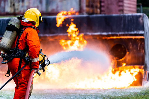 Fire fighter hosing water to extinguish a fire over the car in accident on the road