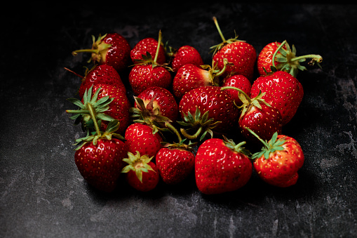 A group of imperfect home grown strawberries arranged into a square shape against a dark marbled backdrop.