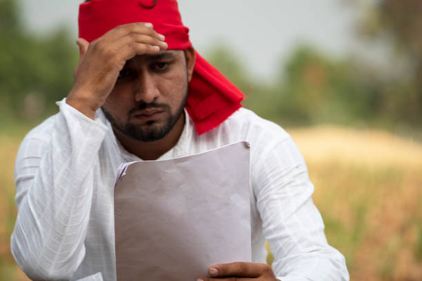 Stressed farmer analyzing finances on agricultural field