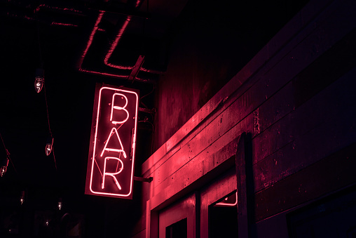 neon BAR sign lights up the doorway of a drinking establishment at night