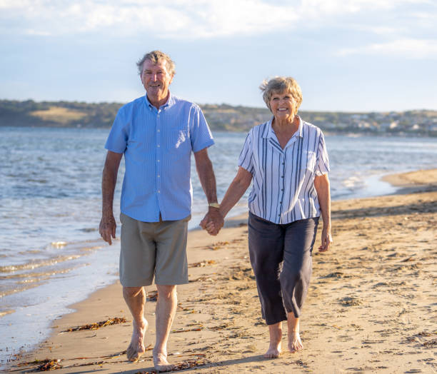 istock Happy senior couple embracing and holding hands walking on empty beach at sunset. Active healthy elderly woman and man on a romantic walk by the sea. Aging together and retirement lifestyle concept. 1256078565