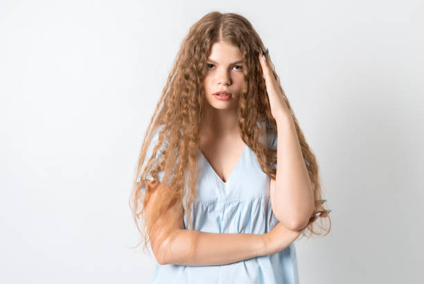 foto de la joven europea cansada con el pelo largo rizado, sostiene su mano cerca de su cabeza, siente fatiga, necesita un buen descanso, tiene expresión dormida, aislada sobre fondo blanco. el cansancio y las personas - middle eastern ethnicity teenage girls women sadness fotografías e imágenes de stock