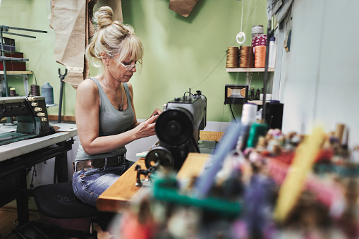 Female blonde dressmaker cloth designer works on sewing machine in her workspace.