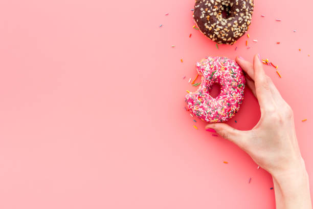 istock Hand holding donut with icing and sprinkles. Flat lay, top view 1256090388