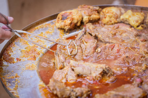 Detail of a human hand turning a pork steak meat cooked in vegetable sauce together with sausages and chicken meat on a barbeque fire in a traditional croatian kotlovina dish.