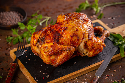 Whole roasted chicken on slate cutting board, ready to served