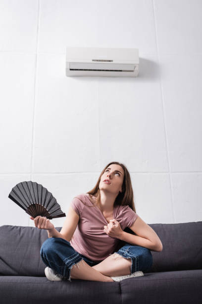 istock young woman suffering from heat and using hand fan at home with broken conditioner 1256098106