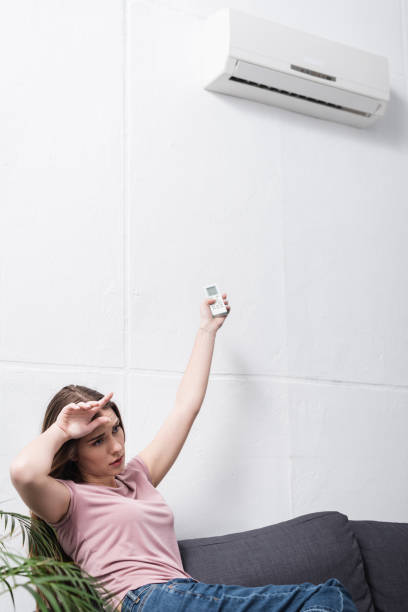 istock exhausted girl suffering from heat while trying to switch on air conditioner 1256098108