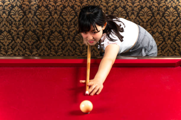 Single billiard cue ball with red dot resting on red pool table felt under dramatic lightingg
