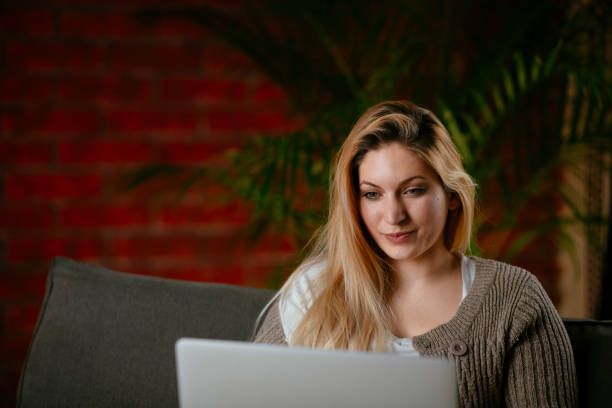 istock Beautiful young woman relaxing on comfortable couch and using laptop at home. 1256102644
