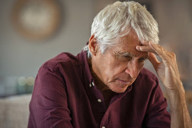 Retired senior man with migraine Tired and stressed old man with hand on head sitting at home with headache. Senior retired man at home feeling worried about health problems. Depressed elderly man sitting at home wit head pain suffers from loneliness. old man depressed stock pictures, royalty-free photos & images