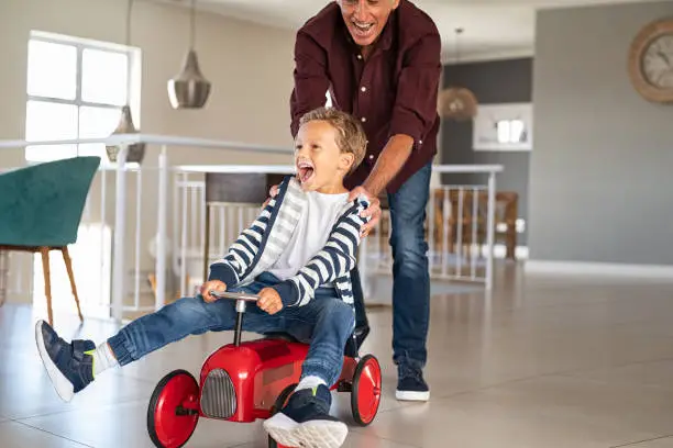 Photo of Playful grandfather pushing grandson toy car