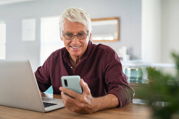 senior mann arbeitet auf laptop und mit smartphone - laptop senior adult computer men stock-fotos und bilder