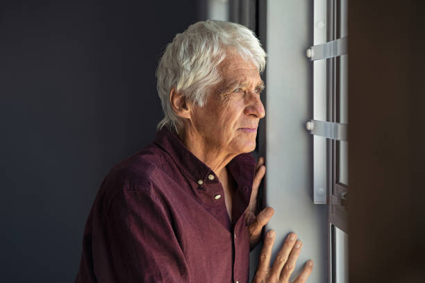 viejo solitario mirando por la ventana - pensive senior adult looking through window indoors fotografías e imágenes de stock