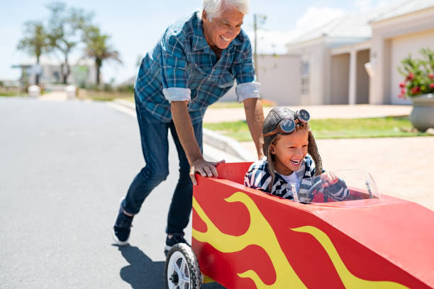 Grandfather pushing his little boy on toy car Senior grandfather helping grandson ride on kids toy car. Happy old man pushing car while boy driving on street. Grandparent playing with little boy on gokart. kid toy car stock pictures, royalty-free photos & images